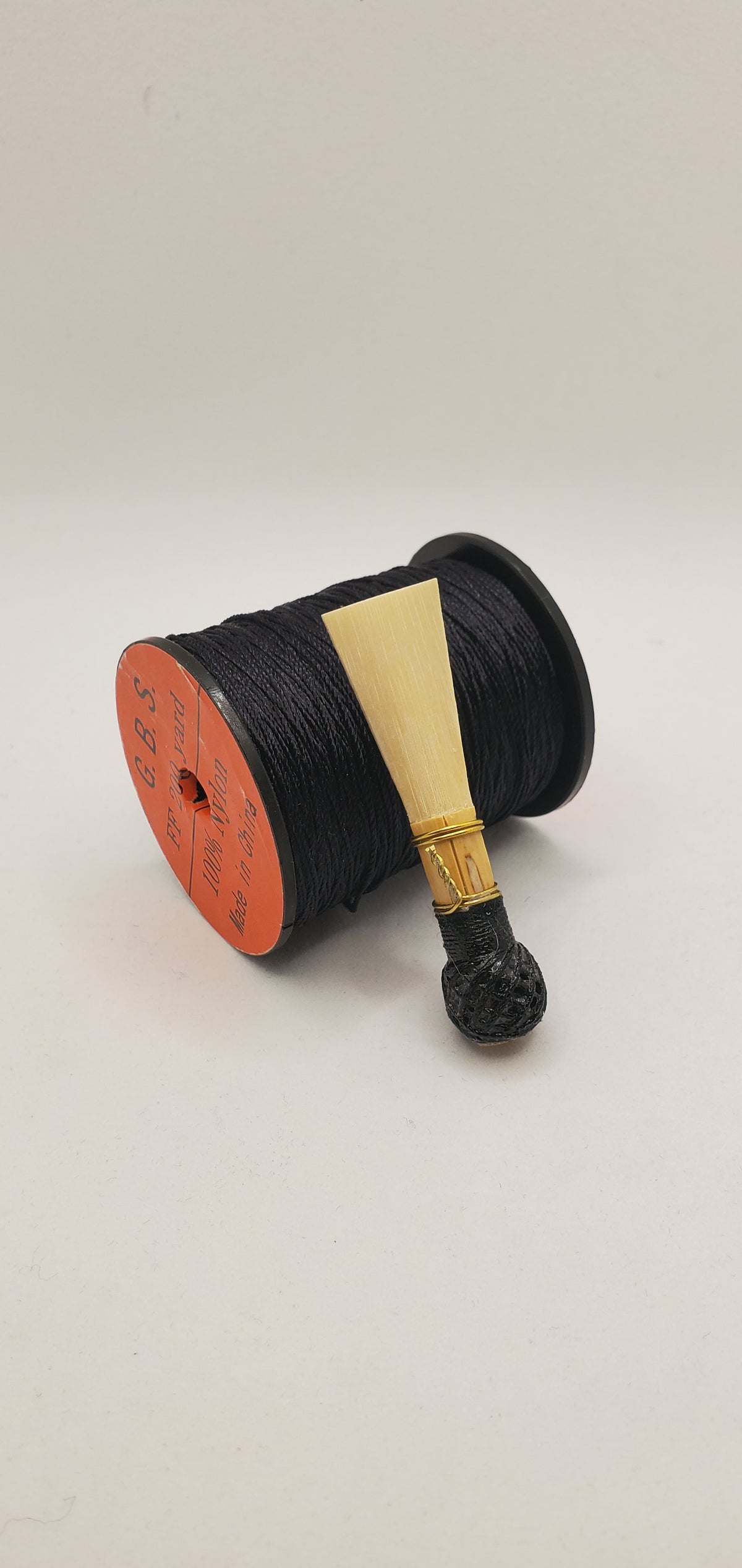 A handcrafted, unfinished bassoon blank with black thread, displayed on a white background.