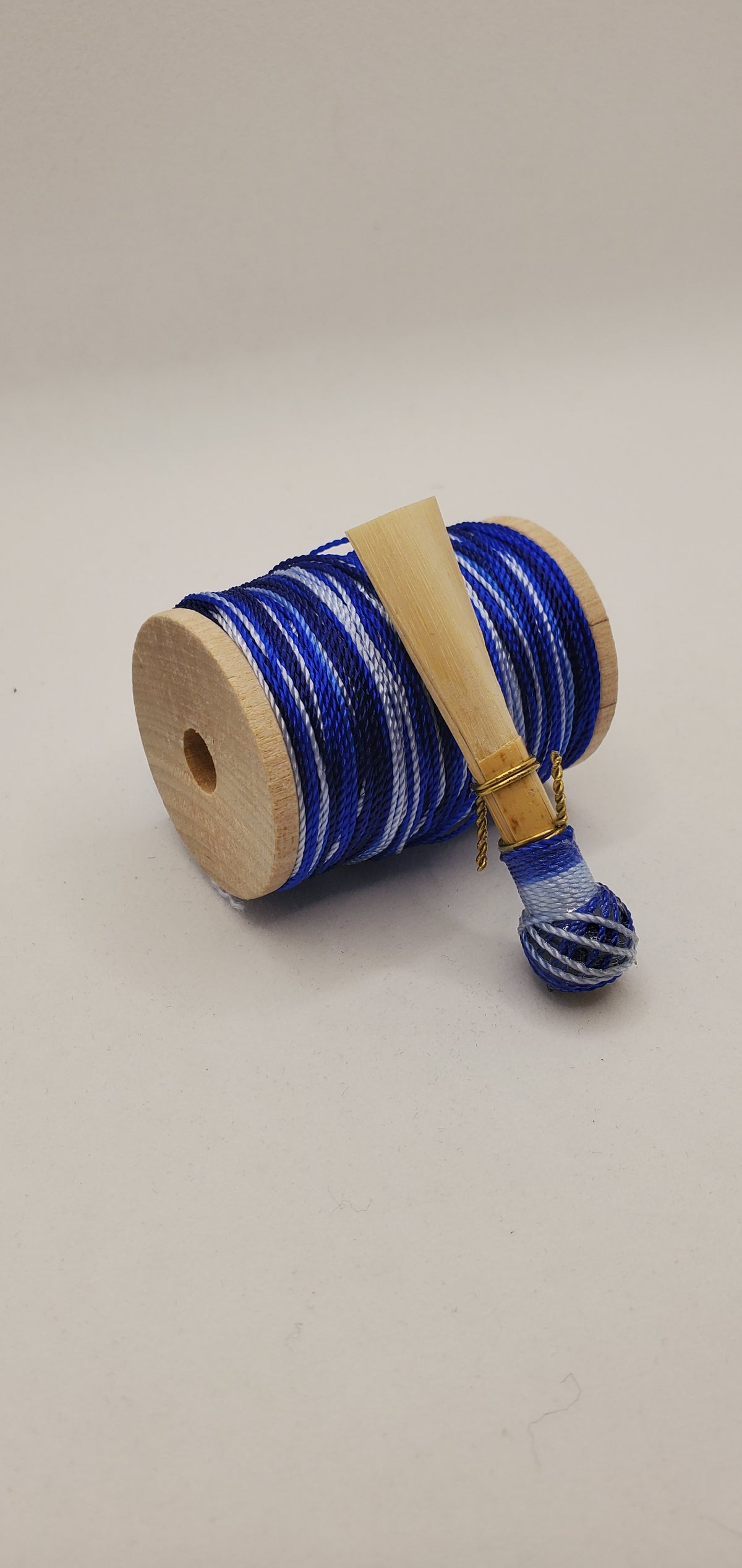 A handcrafted, finished bassoon reed with white, blue, and black thread, displayed on a white background.