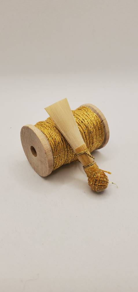 A handcrafted, finished bassoon reed with sparkling gold thread, displayed on a white background.