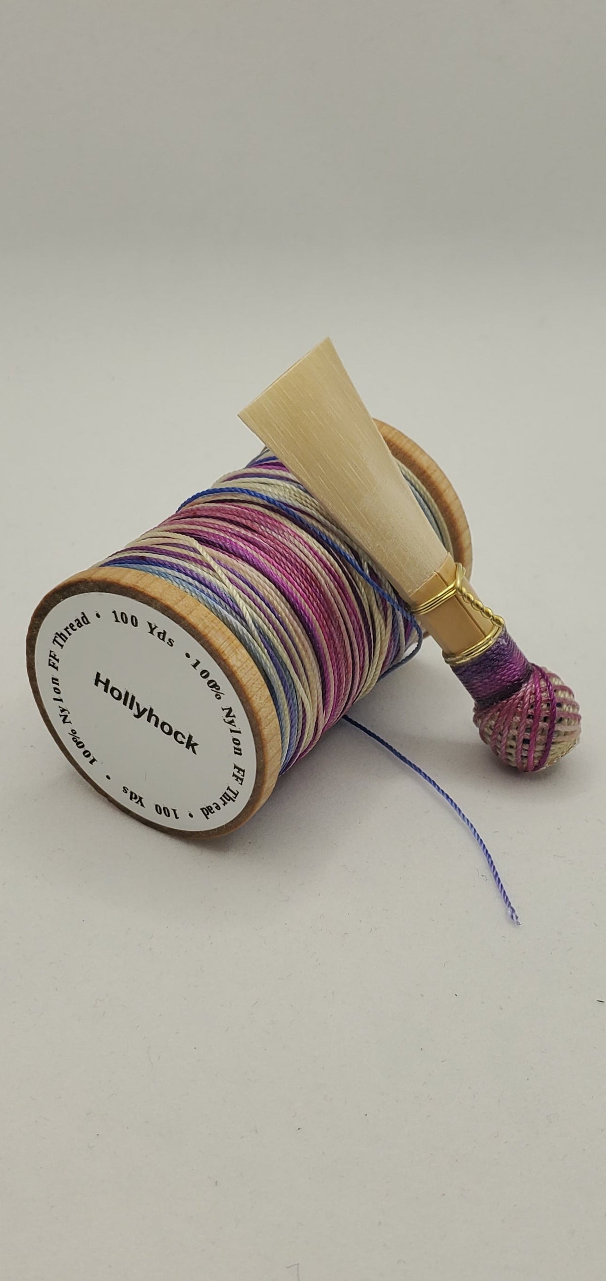 A handcrafted, finished bassoon reed with purple, blue, and tan thread, displayed on a white background.