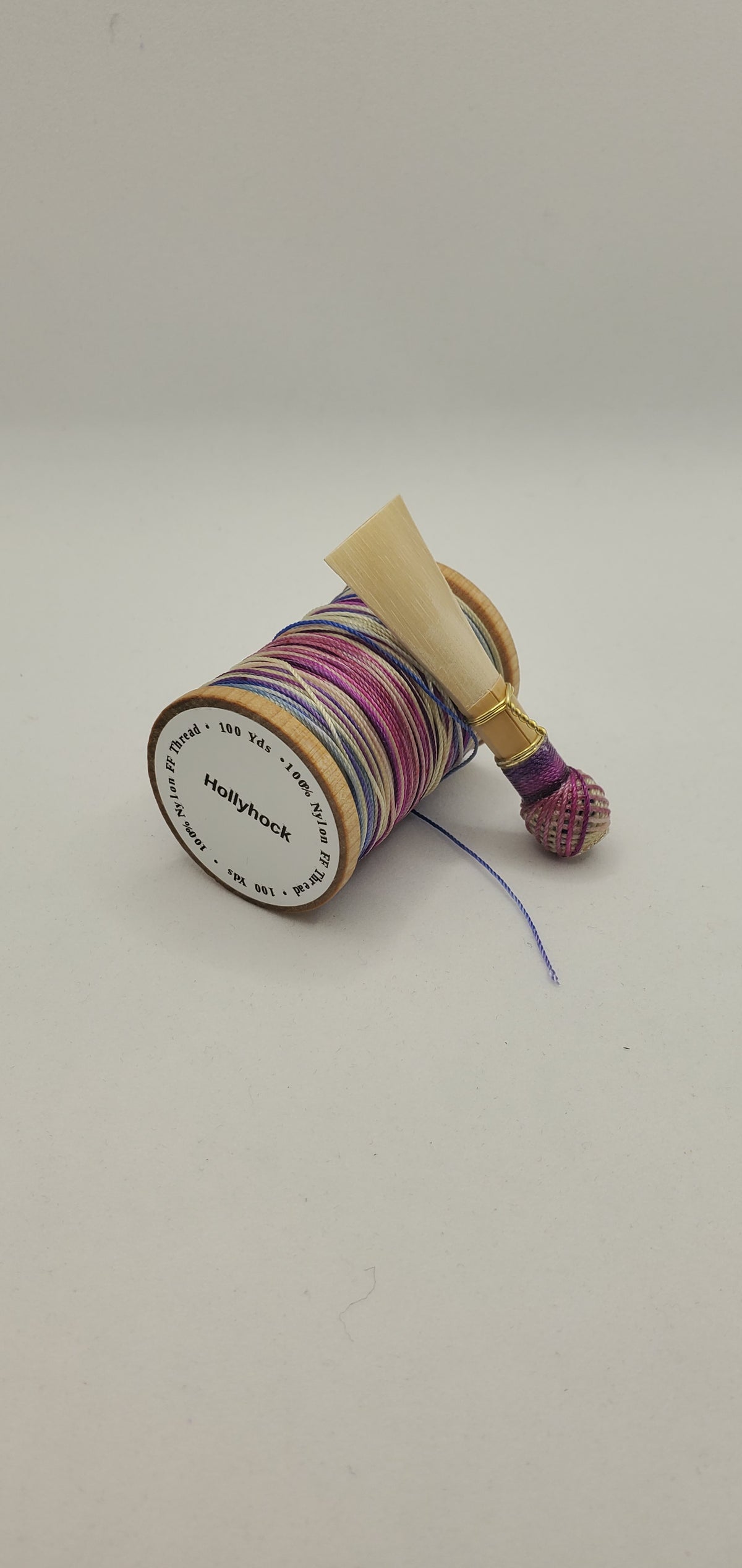 A handcrafted, unfinished bassoon blank with purple, blue, and tan thread, displayed on a white background.