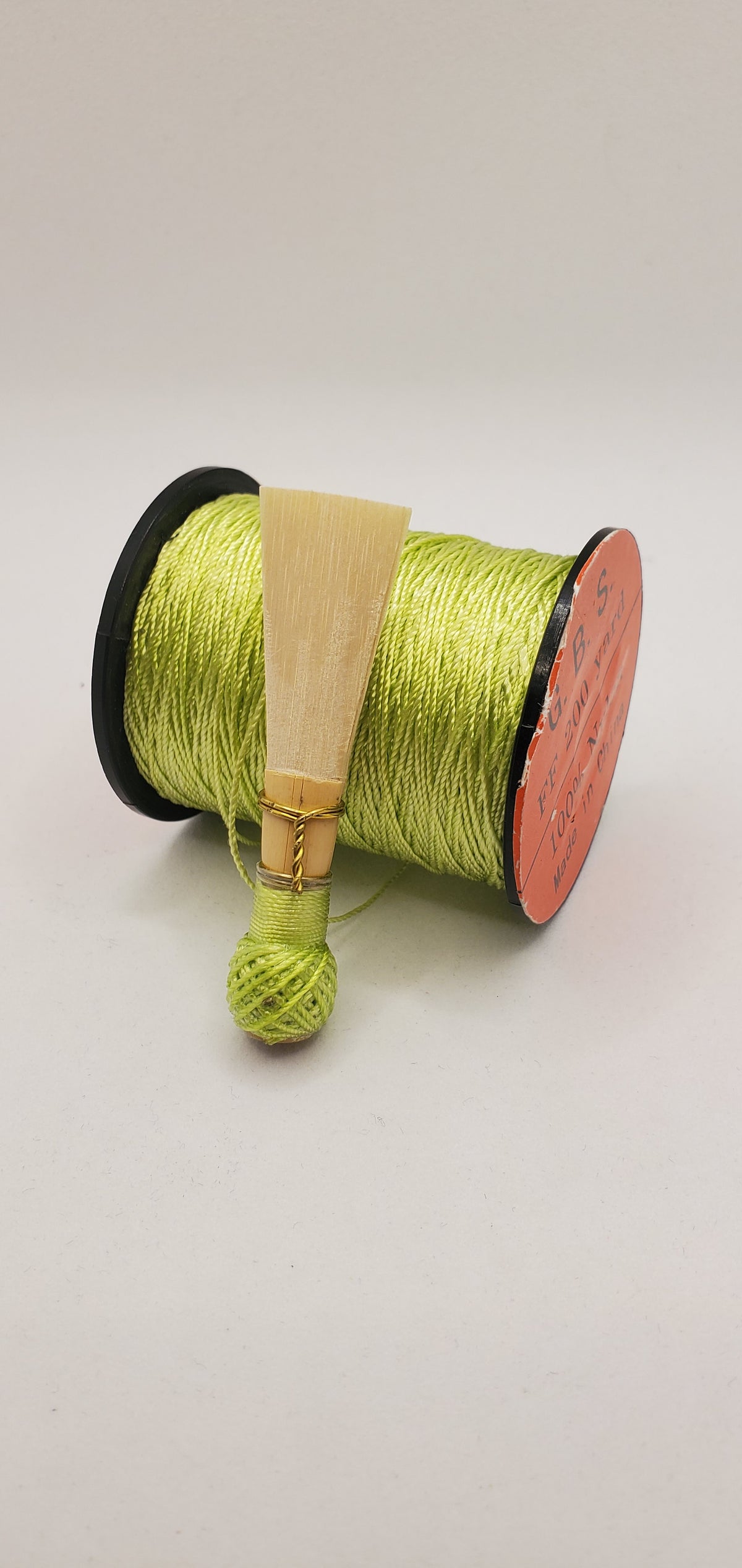 A handcrafted, finished bassoon reed with lime green thread, displayed on a white background.