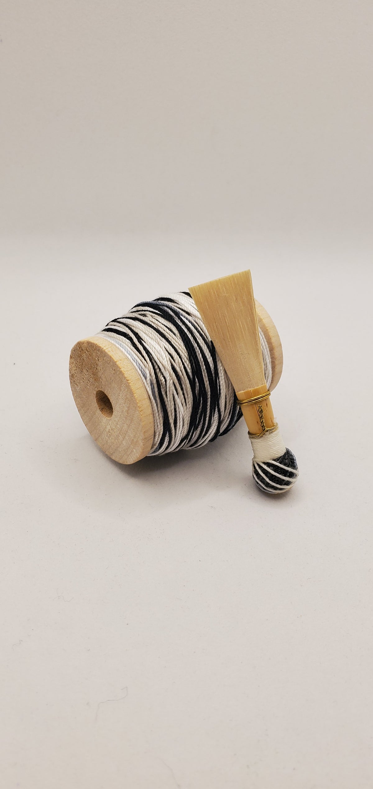 A handcrafted, finished bassoon reed with white and black thread, displayed on a white background.