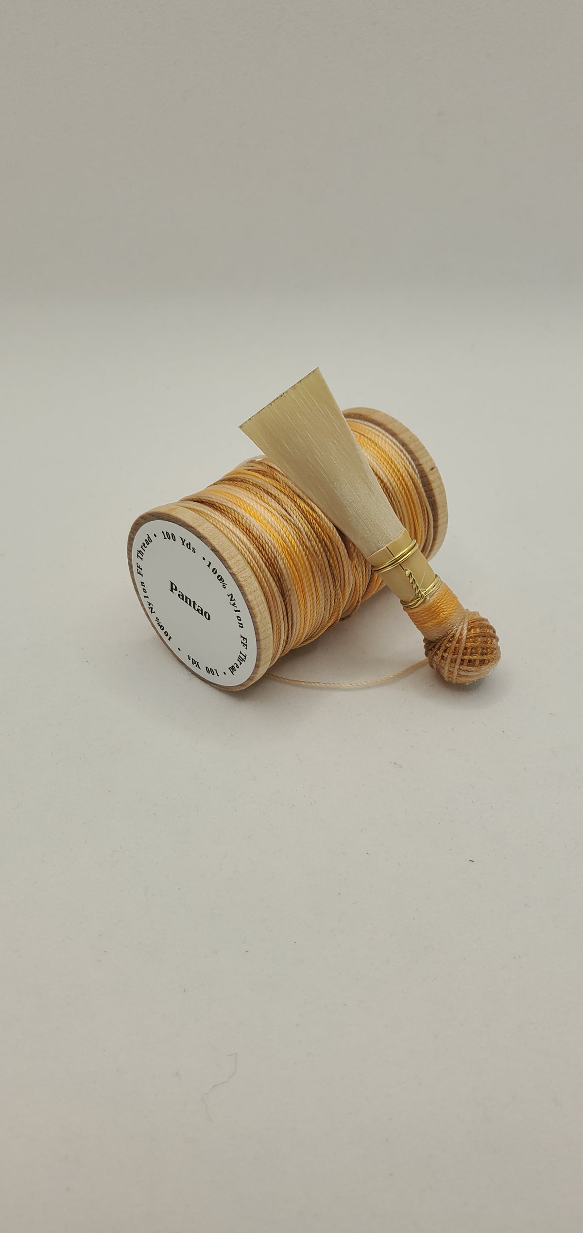 A handcrafted, unfinished bassoon blank with tan, brown, and orange thread, displayed on a white background.
