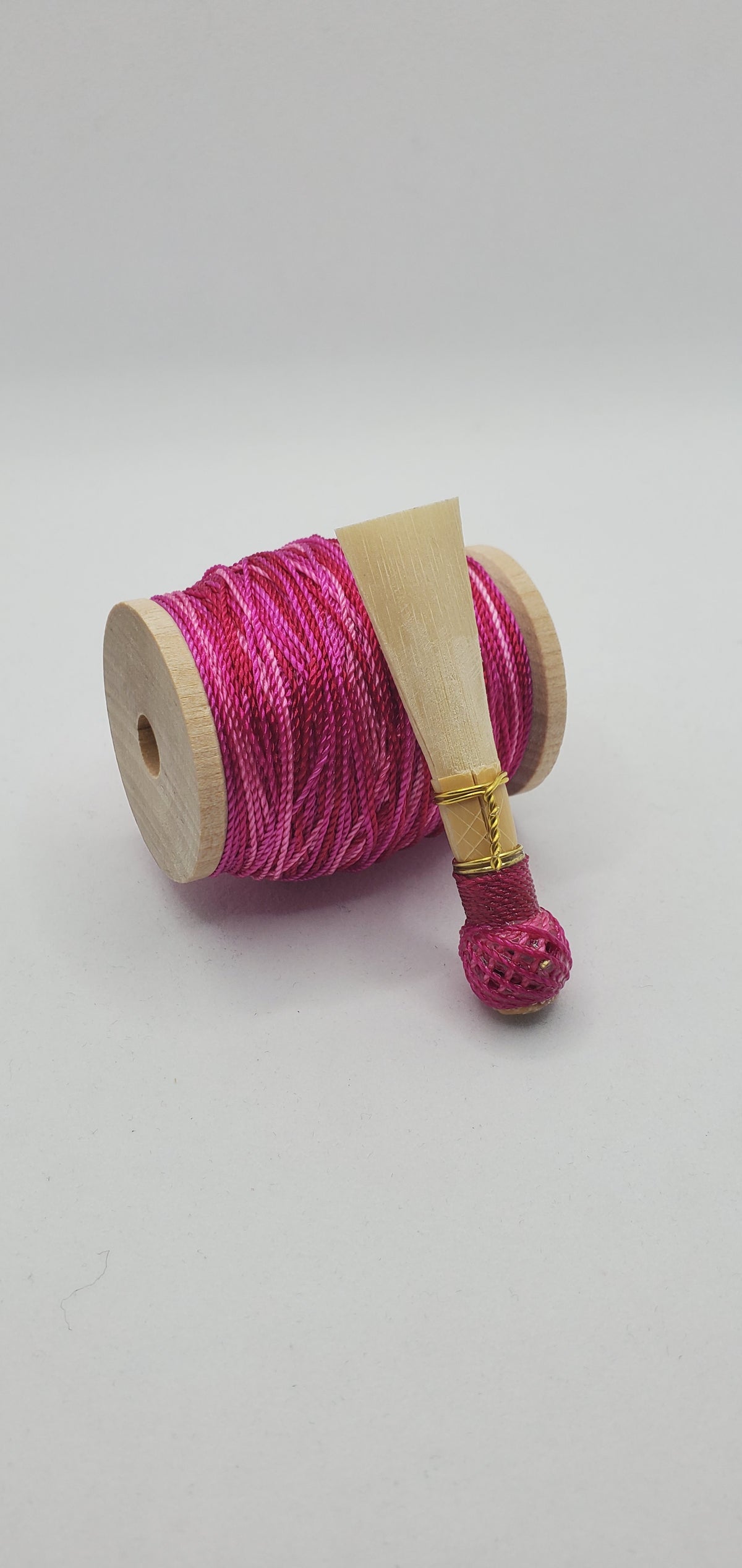 A handcrafted, finished bassoon reed with pink colored thread, displayed on a white background.