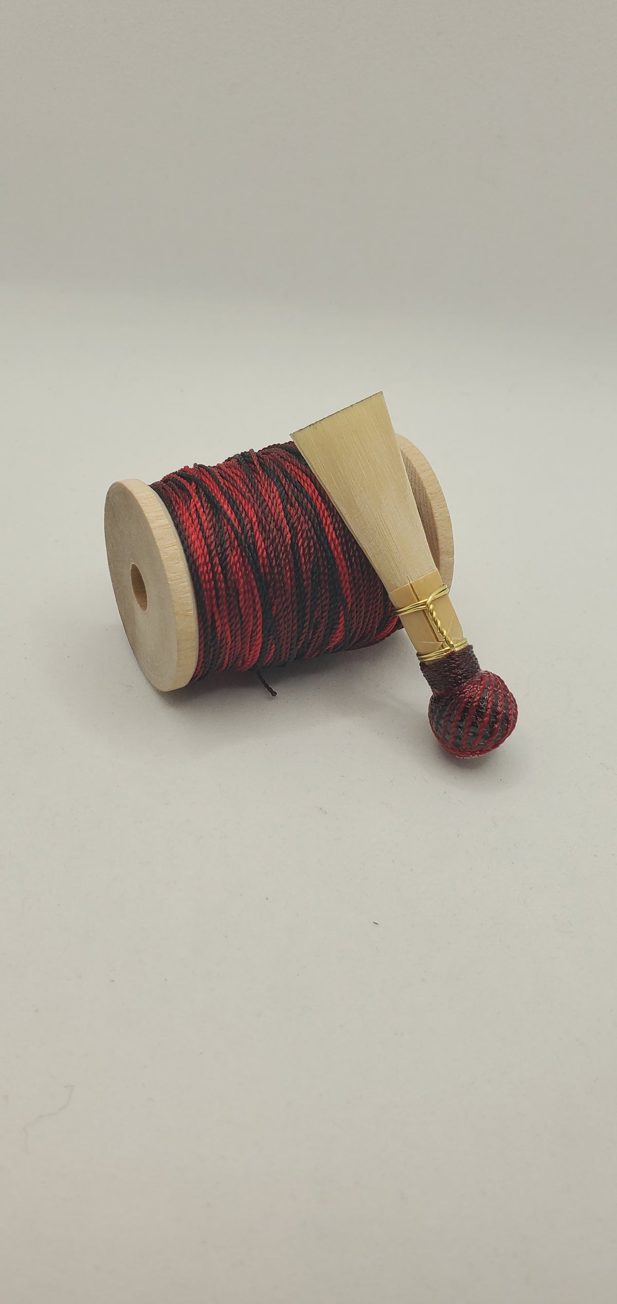 A handcrafted, unfinished bassoon blank with red and black thread, displayed on a white background.
