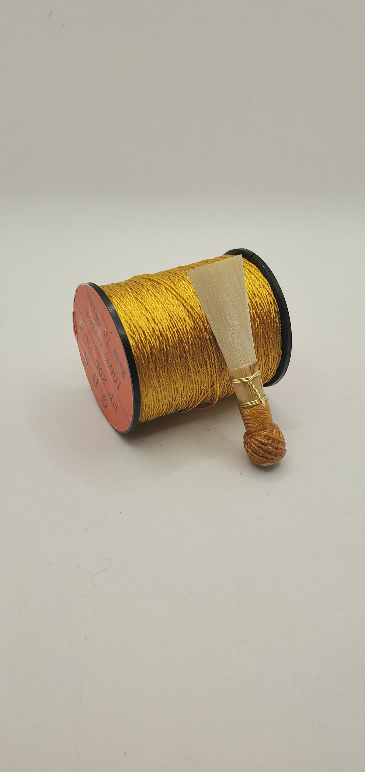 A handcrafted, finished bassoon reed with shiny gold thread, displayed on a white background.