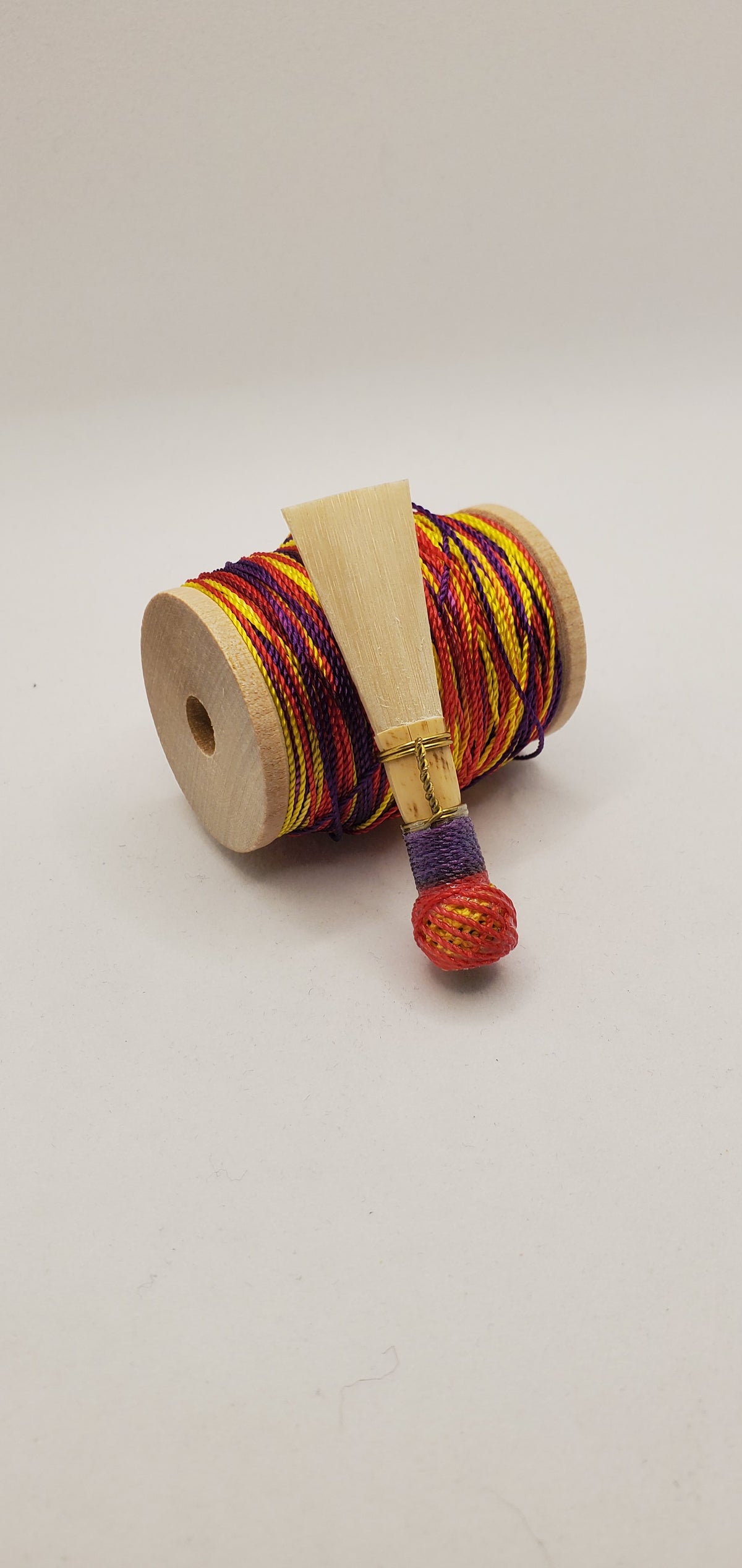 A handcrafted, unfinished bassoon blank with red, yellow, and purple thread, displayed on a white background.