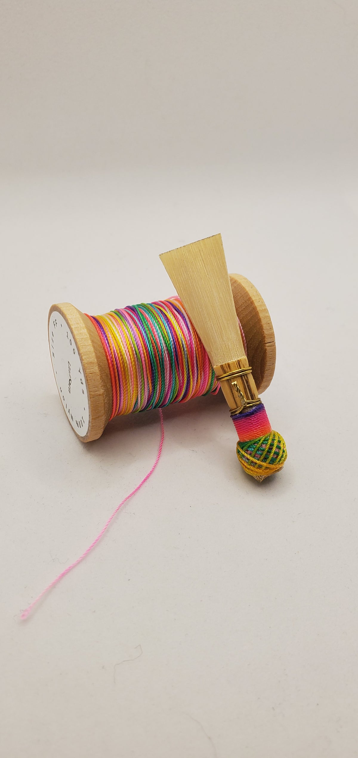A handcrafted, unfinished bassoon blank with light multicolored thread, displayed on a white background.