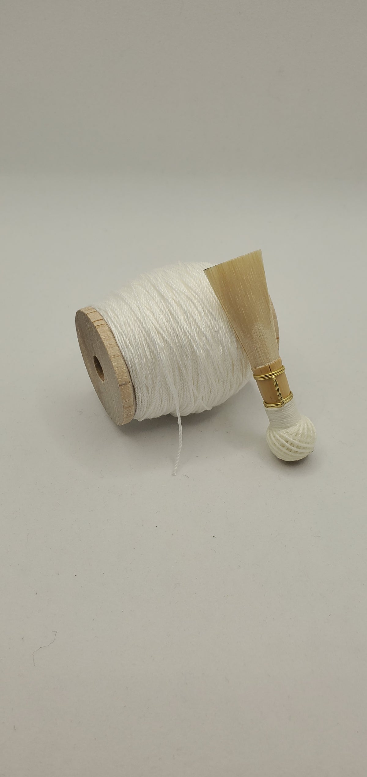 A handcrafted, unfinished bassoon blank with white thread, displayed on a white background.